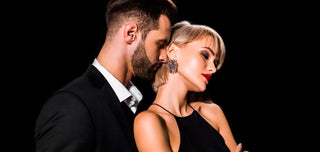 Women's perfumes that drive men crazy. Men and women dressed in black, elegant, on a black background. The man is behind the woman and smells her neck from behind. The woman bends her neck and closes her eyes.