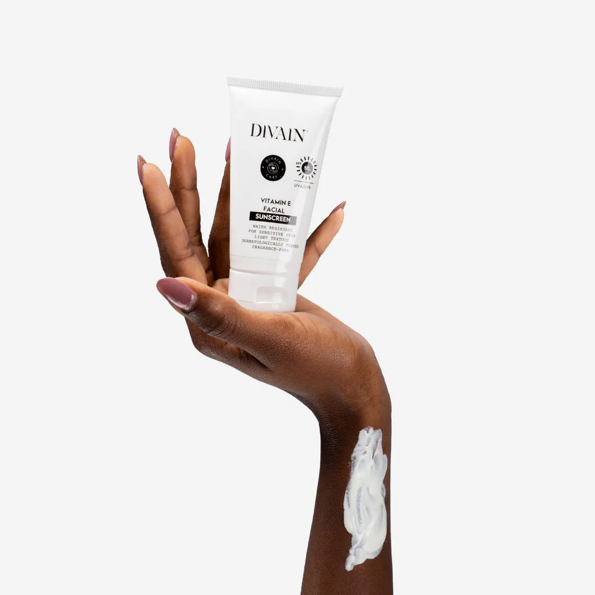 Protector solar facial divain Care con vitamina E sostenido en la mano y textura aplicada en la piel