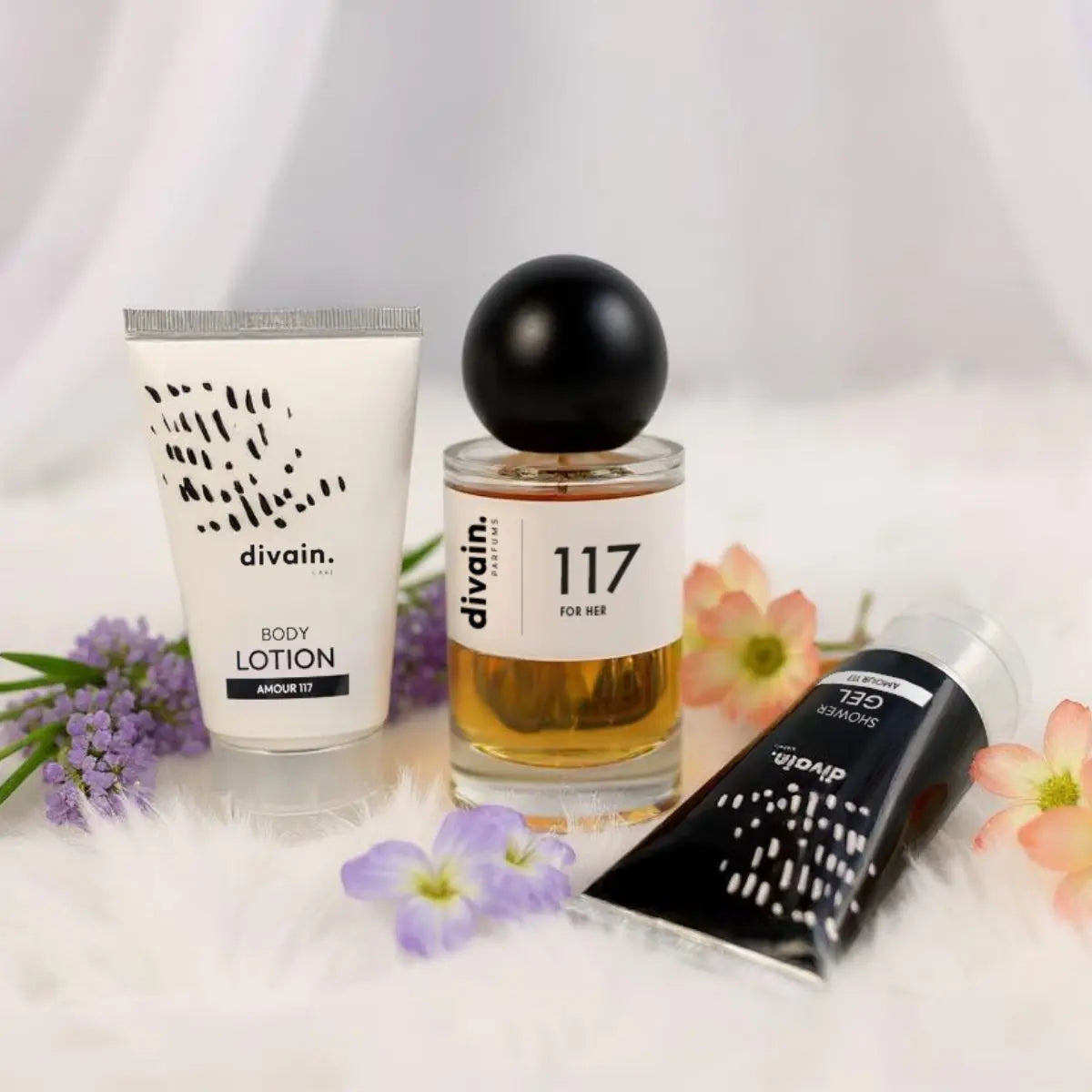 Perfume divain 117 con su crema corporal y su gel sobre un fondo de flores.