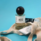 Perfume divain 602 con su crema corporal y su gel dentro de una bolsa de tela sobre un fondo azul.